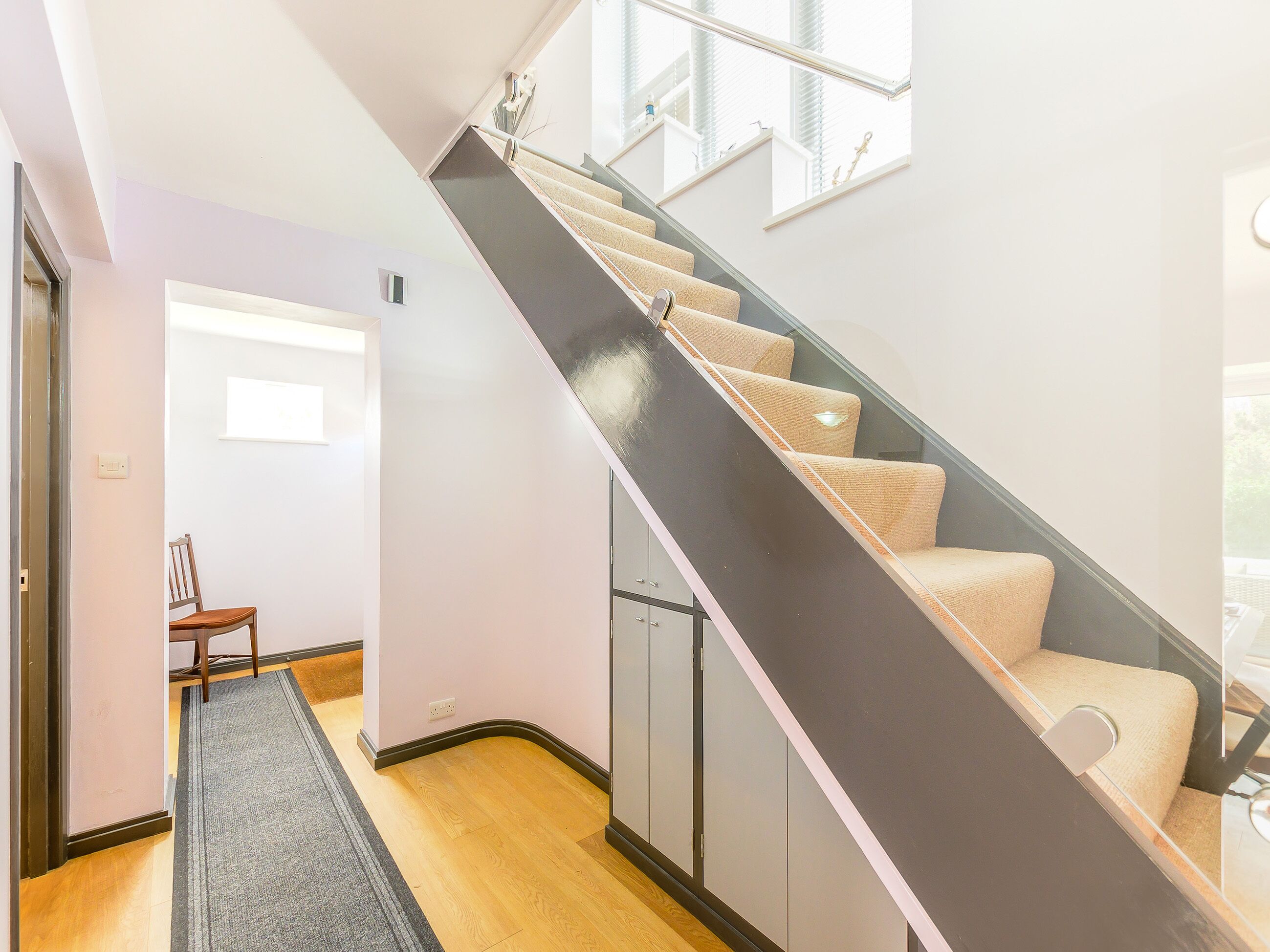 Una escalera moderna con barandilla oscura, escalones alfombrados y vista a una habitación con una puerta y un sillón.