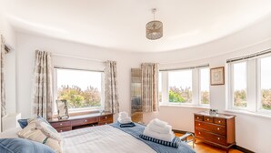 A bedroom with a large bed, a dresser, a mirror, and two windows offering a view of trees. - 4 bedroom accommodation in Elmer (Elmer)