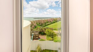 A view from a window overlooking a playground with a slide, a grassy area, and a distant shoreline with a breakwater. - 4 bedroom accommodation in Elmer (Elmer)