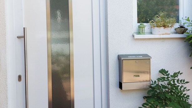 A white door with a vertical glass panel, a small window with plants, and a mailbox on the wall. - Gemütliche Ferienwohnung in Ruhiger Lage (Sachsenheim)