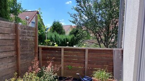 A small outdoor patio with a wooden fence, potted plants, and a blue watering can. - Gemütliche Ferienwohnung in Ruhiger Lage (Sachsenheim)