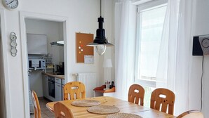 A dining area with a wooden table and chairs, a hanging light fixture, and a view of the kitchen and living area. - Gemütliche Ferienwohnung in Ruhiger Lage (Sachsenheim)