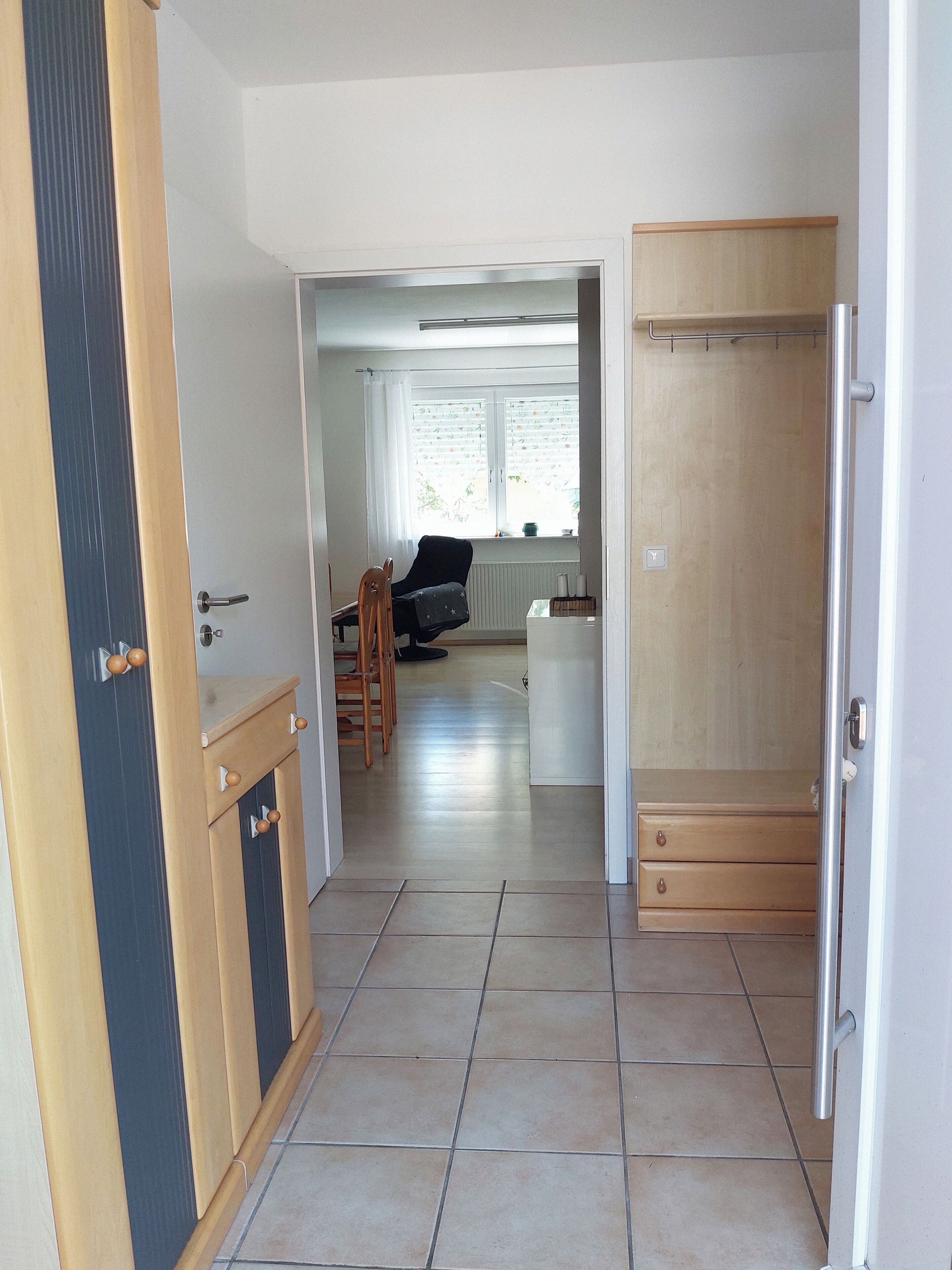 A spacious living area with a dining table and chairs, a black sofa, and a window with blinds.
