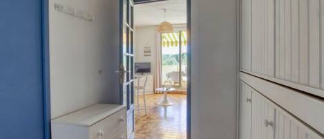 A narrow hallway with a wooden floor, a white dresser, and a view into a dining area with a table and chairs.
