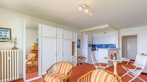 A compact living space with a kitchenette, a dining area, and a seating area with striped chairs. - Les Trois Iles by Interhome (Quiberon)