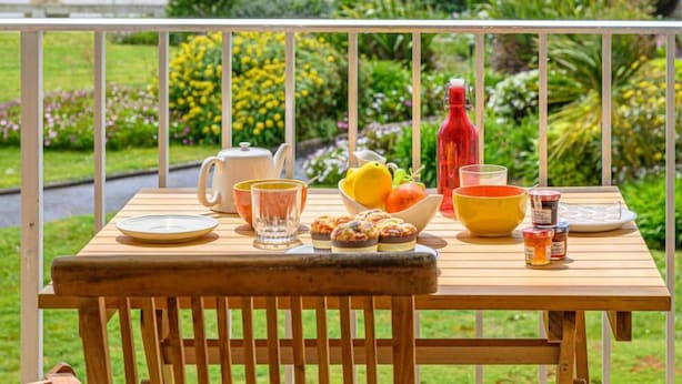 A wooden table with breakfast items on a balcony overlooking a garden and water body. - Les Trois Iles by Interhome (Quiberon)
