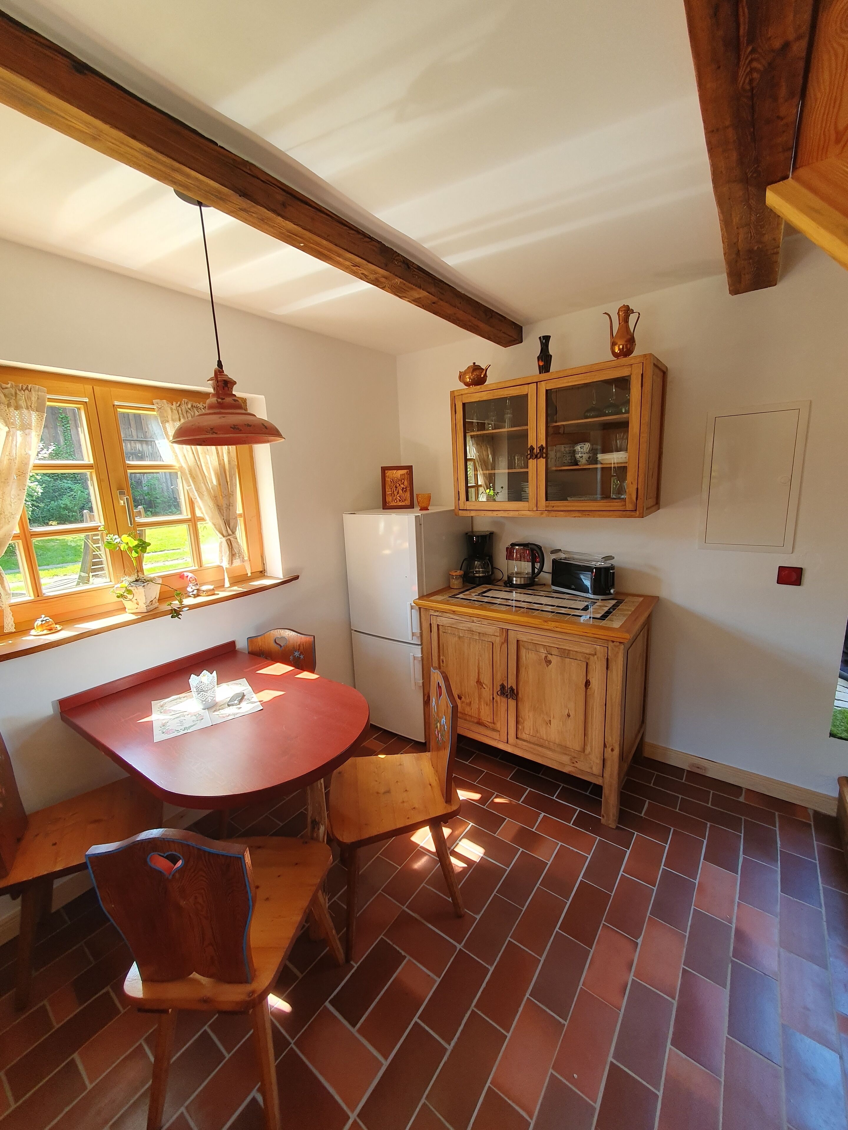 A kitchen with a wooden table and chairs, a refrigerator, a coffee maker, and a cabinet with glass doors.
