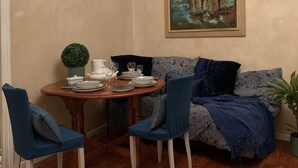 A dining area with a table set for four, a painting of sailboats on the wall, and a sofa with patterned cushions. - La Vie en Rose (Prades)