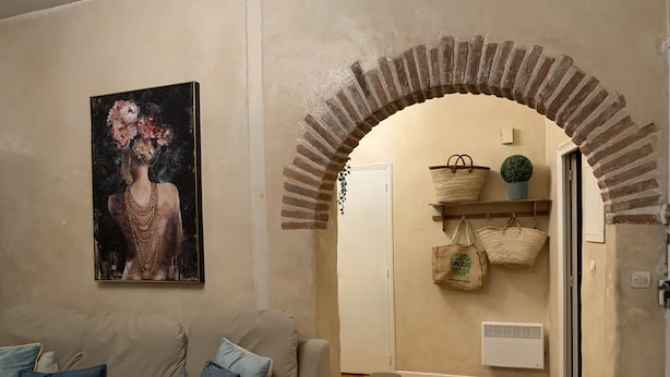 A living room with a beige sofa, a bench, a painting, and a brick archway leading to a door. - La Vie en Rose (Prades)