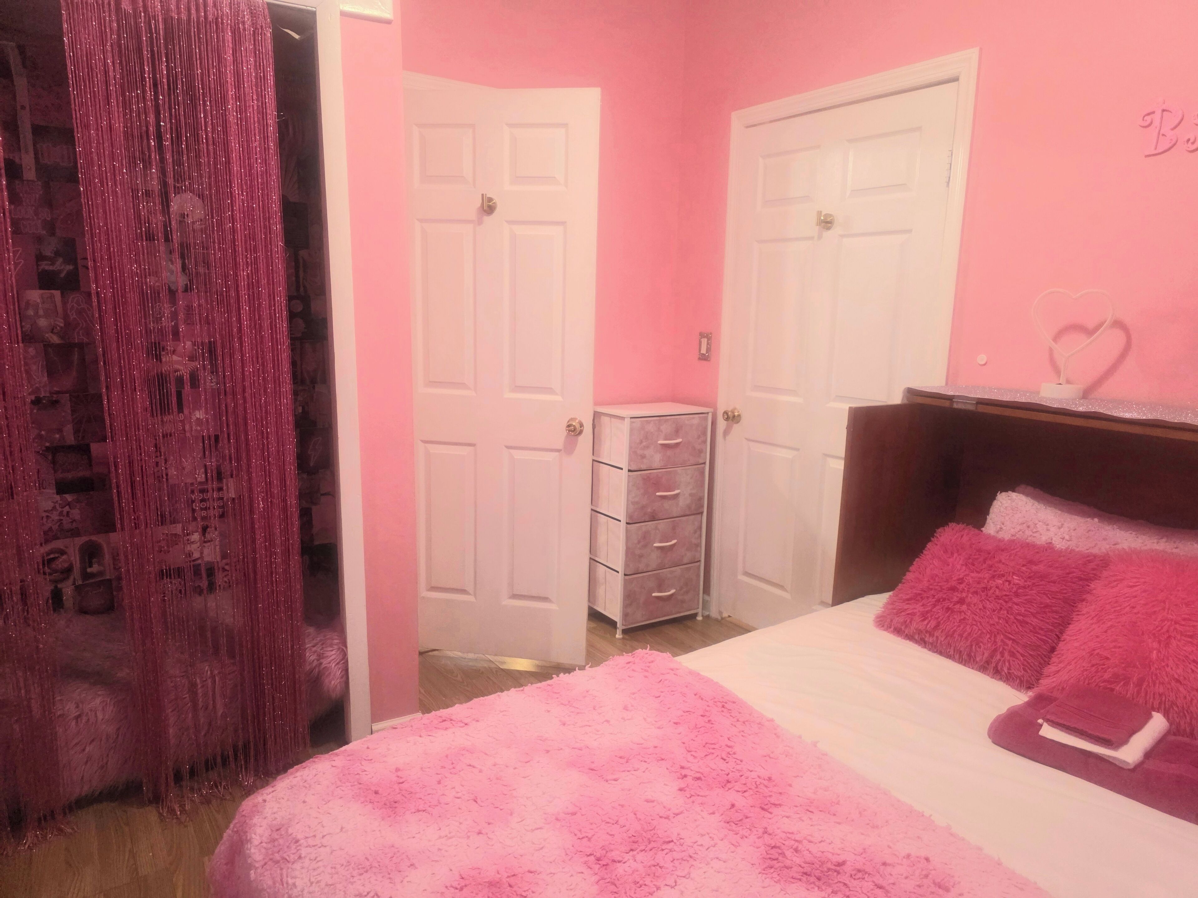 A pink-themed bedroom with a bed, dresser, and two doors.