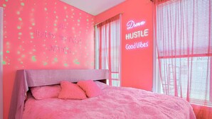 Un dormitorio con temática rosa, que incluye una cama, almohadas y un letrero de neón en la pared.