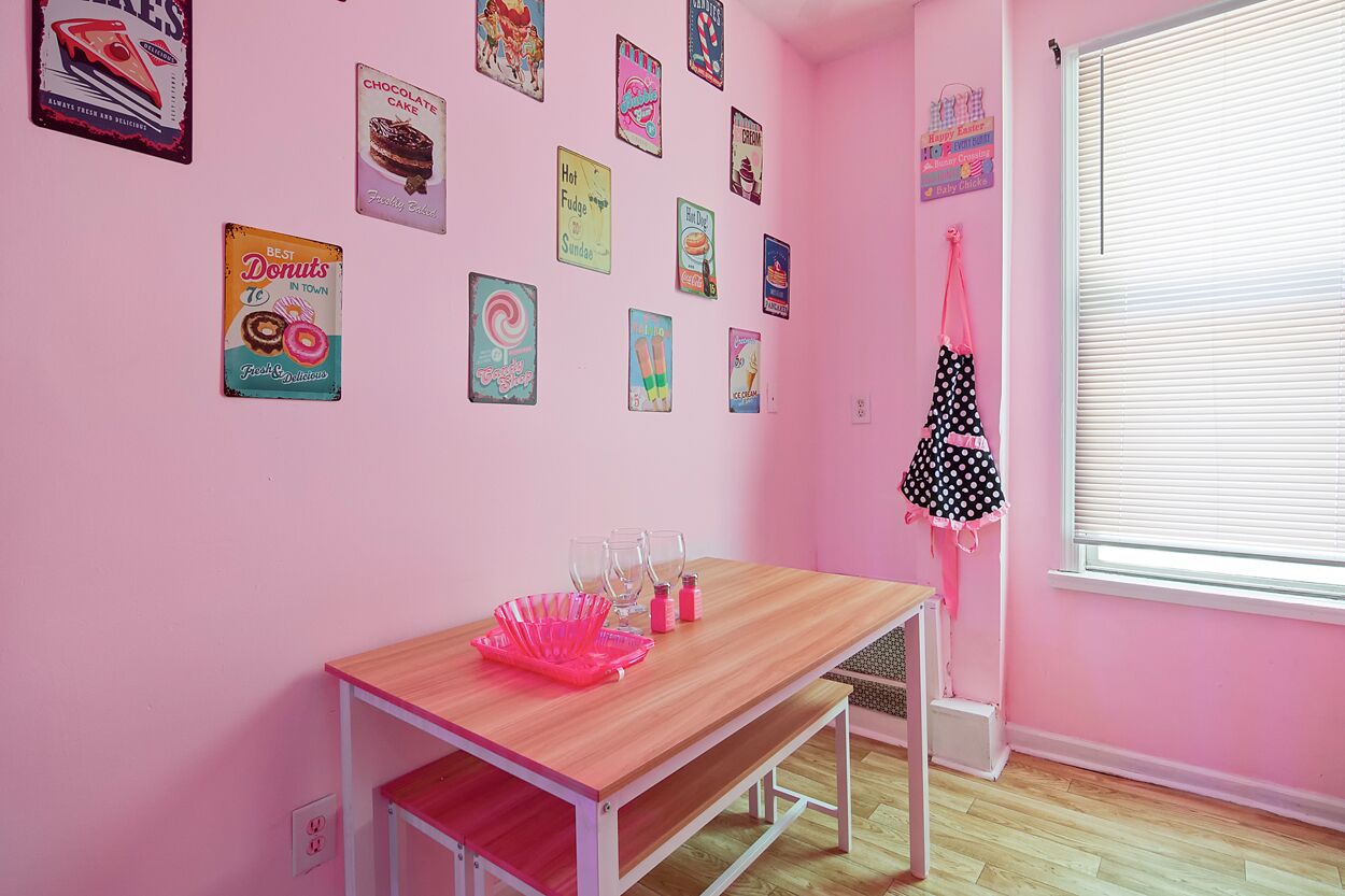 A pink room with a wooden table, pink chairs, and various posters on the wall.