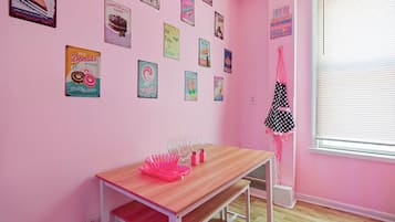 A pink room with a wooden table, pink chairs, and various posters on the wall.