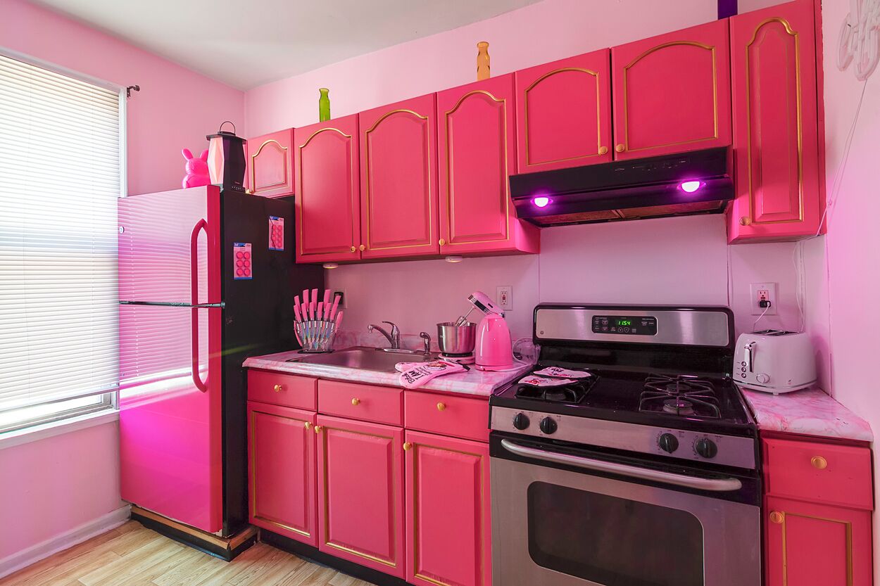 Een keuken met roze kastjes, een zwarte koelkast, een fornuis en een broodrooster.