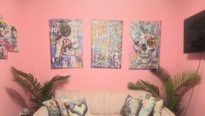 Una habitación con paredes rosas, un sofá color crema, tres obras de arte coloridas y dos plantas en macetas.