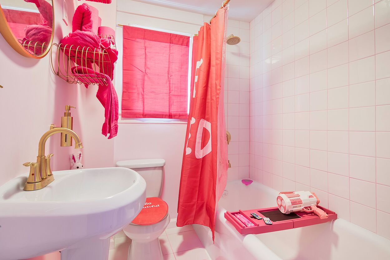 A bathroom with a white sink, a gold faucet, a toilet with a red seat, a shower with a red curtain, and a white bathtub.