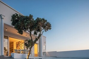 A modern building with a tree in front, a patio with chairs, and a clear sky.