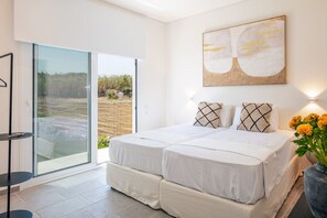 A bedroom with a bed, a sliding glass door leading to an outdoor area, a wall-mounted artwork, and a bedside table with a vase of flowers.