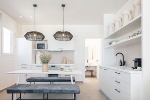 A modern kitchen with white cabinetry, a central island, pendant lighting, and a visible coffee machine.