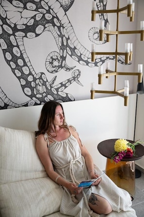 A person sitting on a couch with a large octopus illustration on the wall, a modern chandelier, and a small table with flowers.