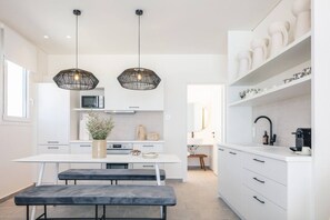 A modern kitchen with white cabinetry, a central island, pendant lighting, and a view into the adjacent dining area.
