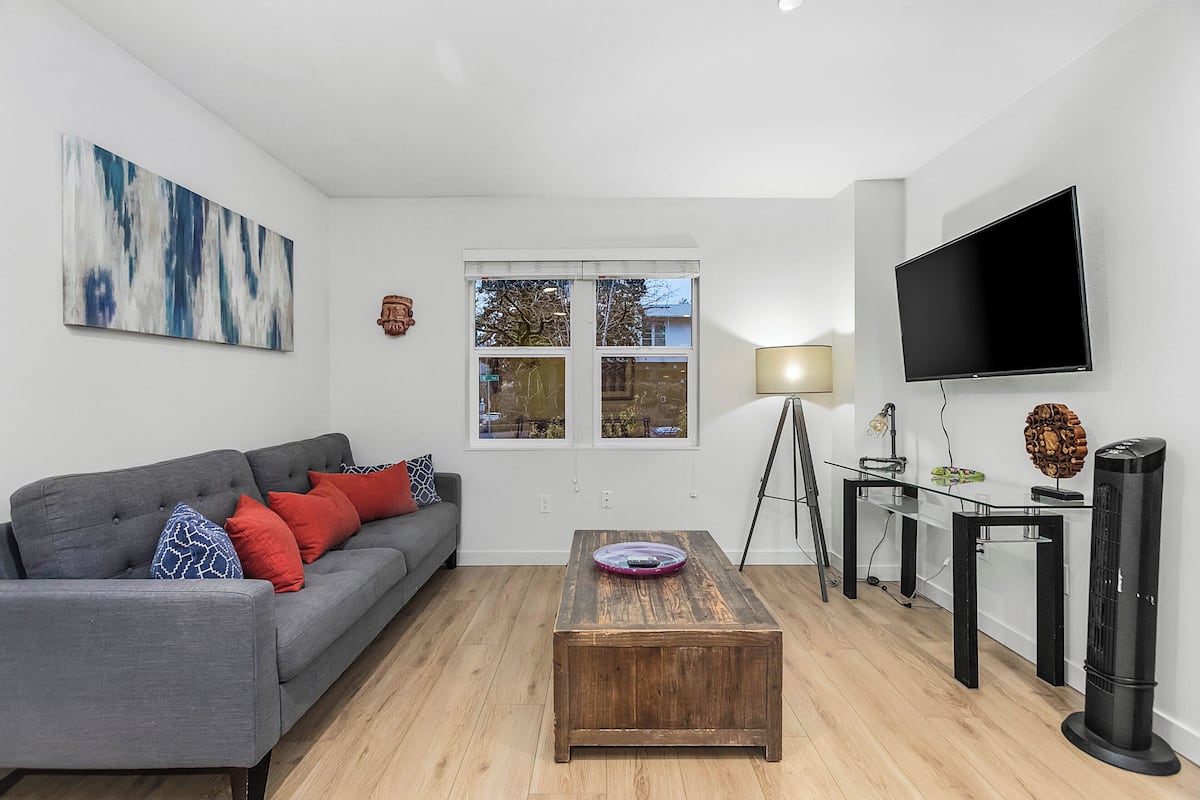 A modern living room with a grey sofa, wooden coffee table, and a flat-screen TV.