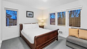 A bedroom with a wooden bed, a gray sofa, and large windows with views of trees and a house. - The Sweetest Hill - 81 Walkscore (Seattle)