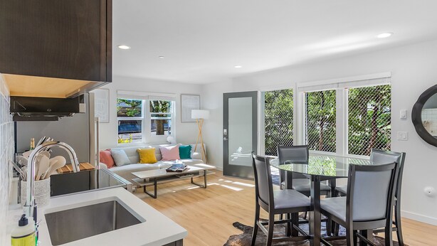 A modern kitchen with a built-in sink, dining area with a glass table and chairs, and a cozy seating area with a sofa and cushions. - The Sweetest Hill - 81 Walkscore (Seattle)
