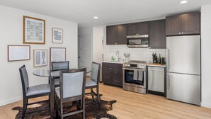 A modern kitchen with dark cabinets, stainless steel appliances, and a glass dining table with chairs. - The Sweetest Hill - 81 Walkscore (Seattle)