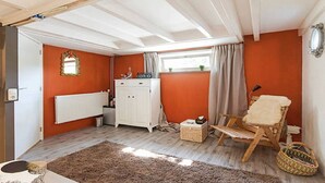 Et værelse med trægulv, en radiator, et hvidt skab, en stol og et vindue med gardiner.