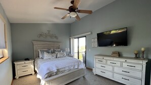 A bedroom with a bed, nightstands, a dresser, a ceiling fan, a TV, and a window with a view. - Incredible Views from Smith Point (Bradley)