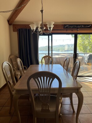 Enjoy meals with a serene view of the lake and forest from this dining area, featuring a large table and comfortable seating for six.