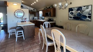 A spacious kitchen with wooden cabinets, a dining area with white chairs, and a large painting on the wall. - Incredible Views from Smith Point (Bradley)