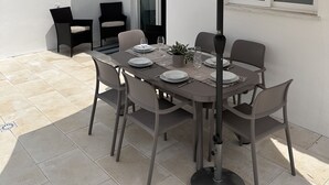 A patio with a table set for four, surrounded by chairs, under a large umbrella. - Cosy refurbished 3 bedroom Vila in a quiet area 2km  from town center (Lagos)