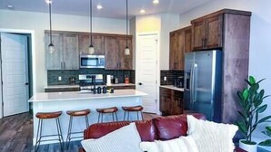 A modern kitchen with wooden cabinets, a central island with bar stools, a stainless steel refrigerator, and pendant lighting. - Inviting Townhouse at Purgatory (Durango)