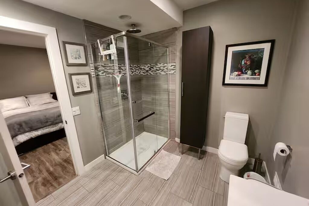 Ein modernes Badezimmer mit einer Duschkabine aus Glas, einer Toilette und einem Bett im angrenzenden Raum.