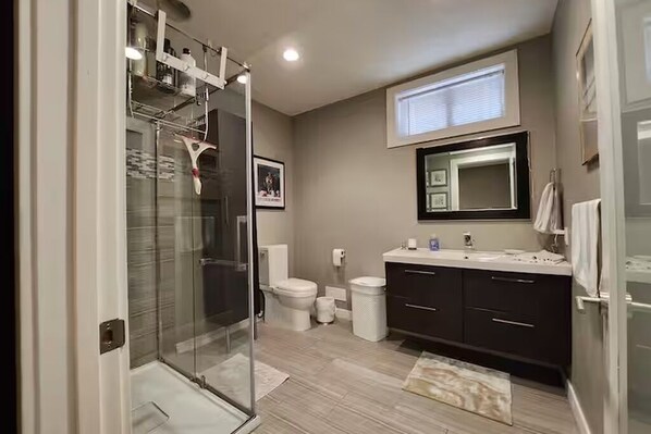 Een moderne badkamer met een douchecabine van glas, een toilet, een wastafel met spiegel en een donkerd badkamermeubel.