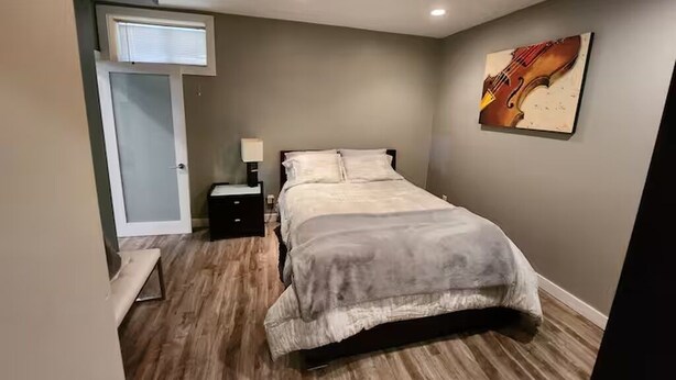 A bedroom with a bed, bedside table, lamp, and a painting on the wall.