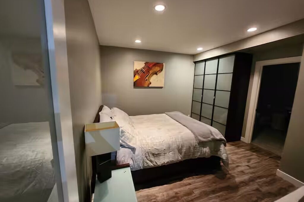 A bedroom with a bed, a painting, a wardrobe, and a door leading to a balcony.
