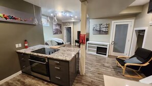A kitchen with a built-in stove, a dining area with a table and chairs, and a living space with a sofa and a chair.