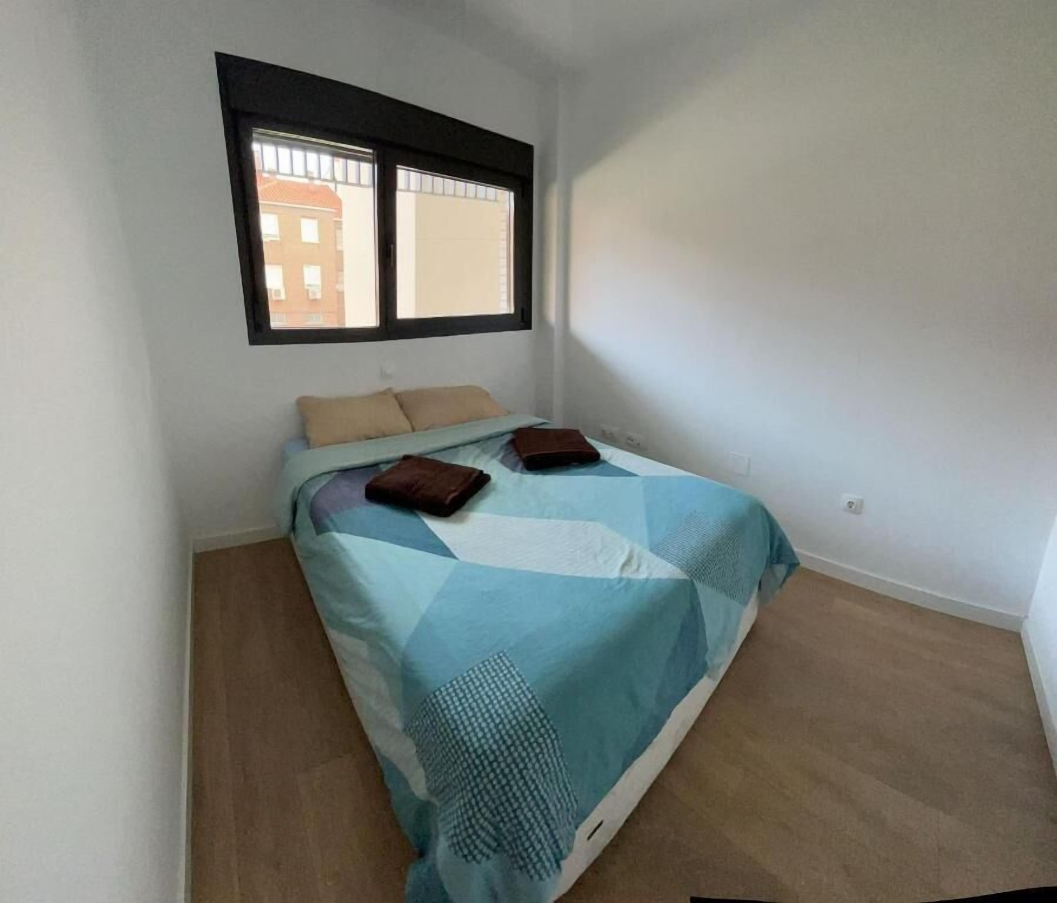 A small, single-bed room with a window, a plain wall, and a carpeted floor.