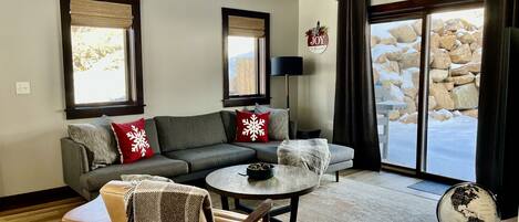 A cozy living room with a grey sofa, red and white snowflake pillows, a wooden chair, a small round table, and a globe on a side table.