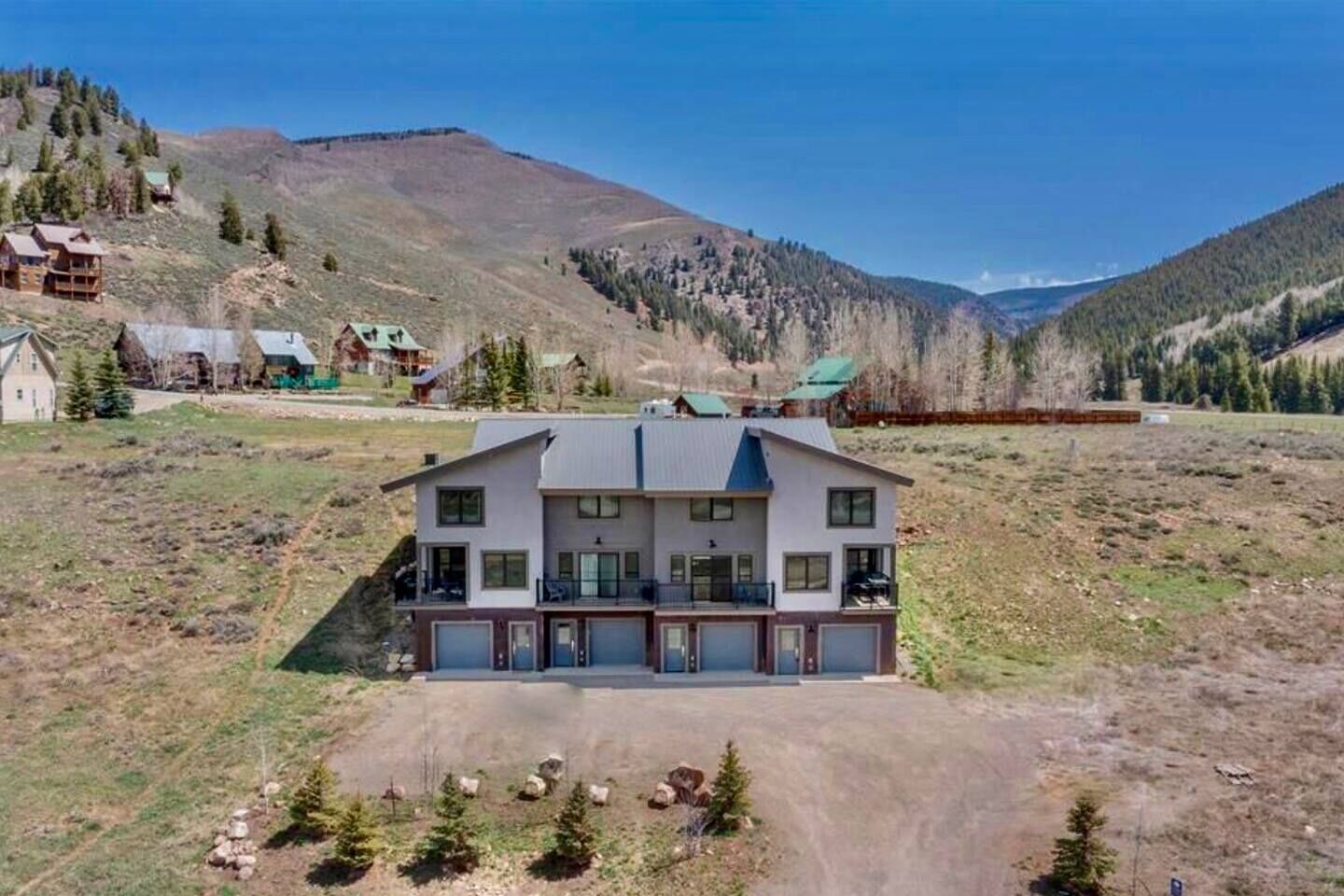 Une maison moderne à deux étages, dotée d’un grand garage et entourée d’un paysage montagneux.