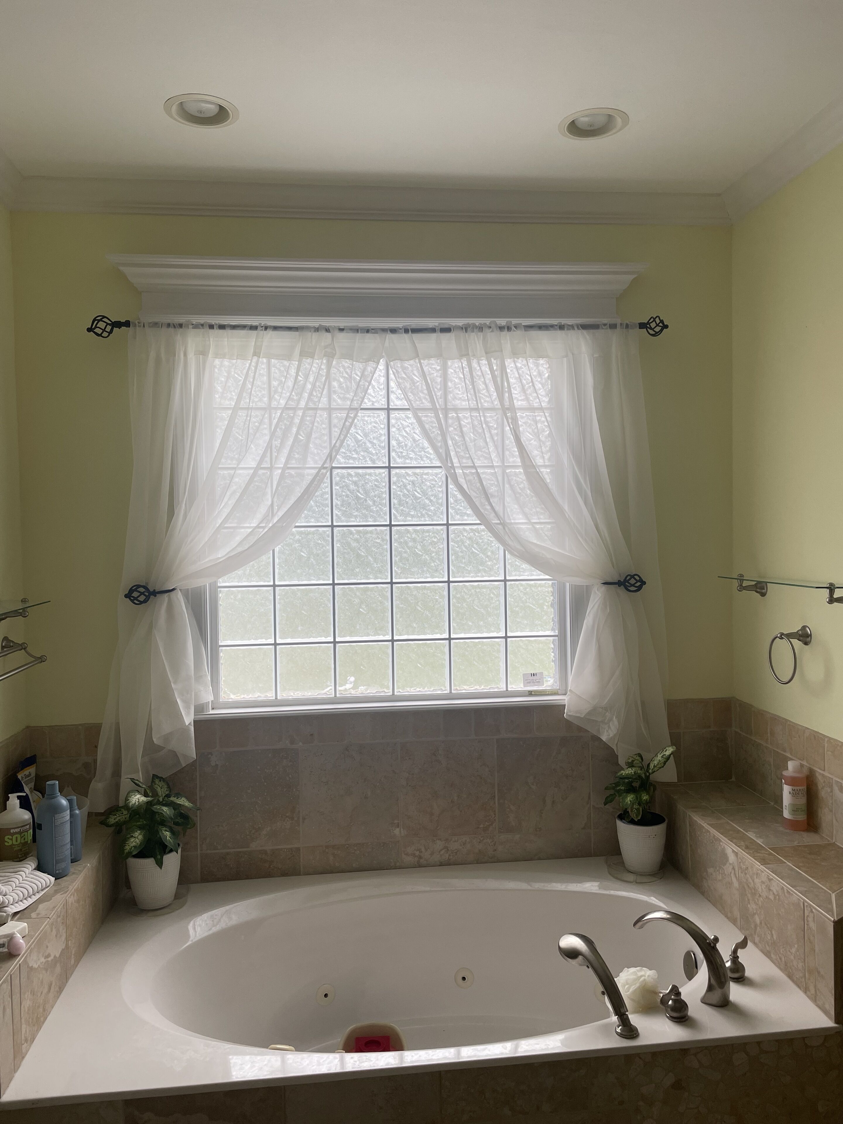 A bathroom with a large bathtub, a window with sheer curtains, and a potted plant.