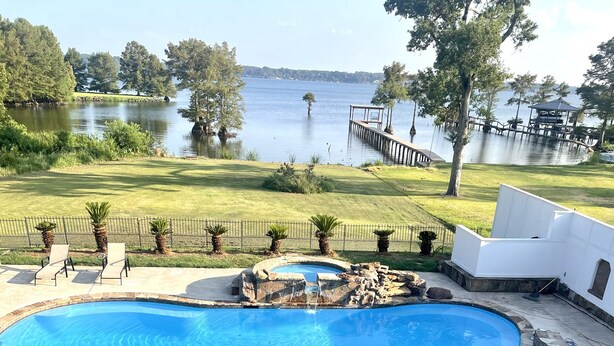 A swimming pool with a curved design, surrounded by a stone deck and a few lounge chairs. - Poolside Paradise on Cross Lake (Shreveport)