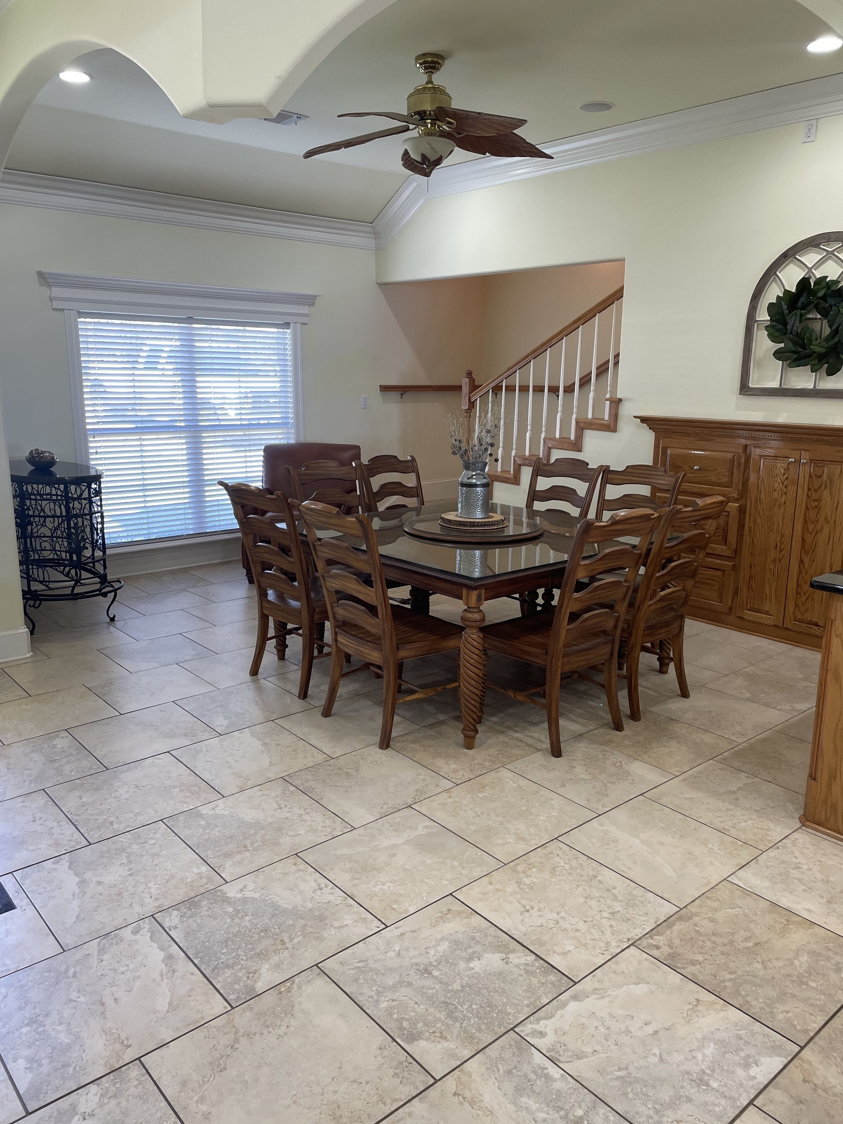 A dining area with a round table, wooden chairs, a ceiling fan, and a staircase.