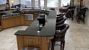 A spacious kitchen with a large island, wooden cabinets, and a stainless steel trash can. - Poolside Paradise on Cross Lake (Shreveport)