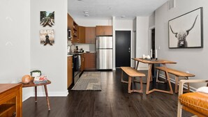 A modern kitchen with wooden cabinets, a stainless steel refrigerator, and a dining area with a wooden table and bench. - The Found Boutique 1 bdrm haven for relaxation. (Traverse City)