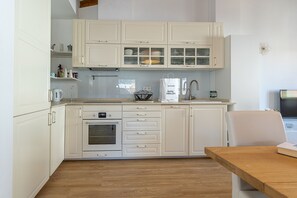 A modern kitchen with white cabinetry, a wooden countertop, and a dining area with a table and chair.