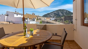 A round wooden table with a beige umbrella, a bottle of wine, and a glass on a balcony overlooking a mountainous landscape. - Townhouse with puig de Maria view by home villas 360 (Pollensa)
